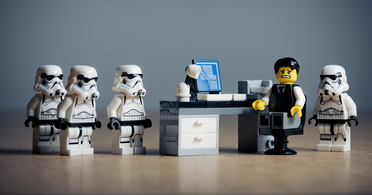 Lego storm troopers standing next to a scared office worker at his desk.